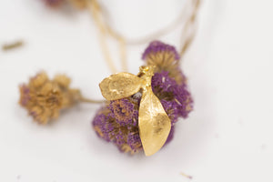 A yellow gold seedling leaf pendant draped across an arrangement of dried flowers